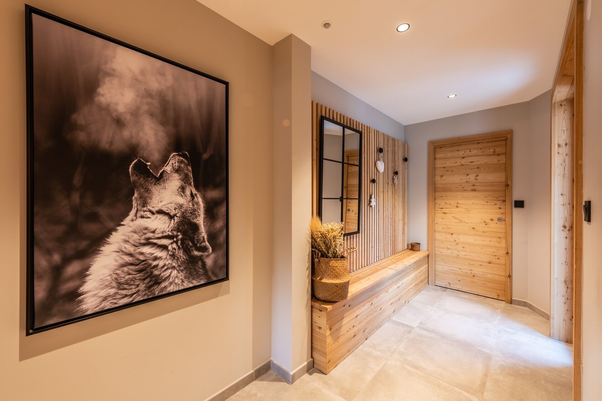 A hallway with a framed photograph, a wooden bench with a vase, a mirror, and a wooden door.
