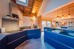 A modern kitchen with wooden beams, a large island, and a view to the outside. - Malago - Five Bedroom Chalet, Sleeps 14 (Le Monêtier-les-Bains)