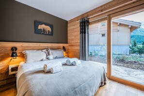 Ein Schlafzimmer mit Holz-Kopfteil, einem Bett mit weißer Bettwäsche, einer Gartenzwerg-Dekoration und einem großen Fenster mit Blick auf ein Gebäude und Bäume.