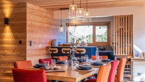 Un'area pranzo con un tavolo in legno apparecchiato per quattro persone, circondato da sedie rosse e illuminato da lampade pendenti a sospensione.