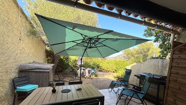 An outdoor patio with a wooden table, chairs, a green umbrella, and a barbecue grill. - Le Cocody - Appt avec terrasse, proche de la plage (Lumio)