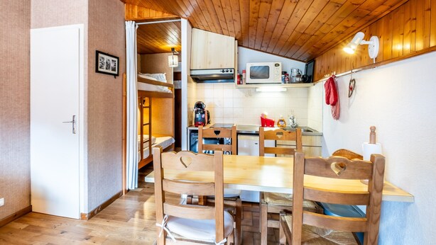 Cocina compacta con armarios de madera, microondas y comedor con mesa y sillas.