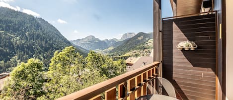 A balcony with a view of mountains, a wooden railing, and a table with a chair.