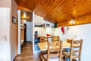 Un interior de madera con una mesa y sillas de comedor, una zona de cocina con microondas y una puerta visible que da a otra habitación.