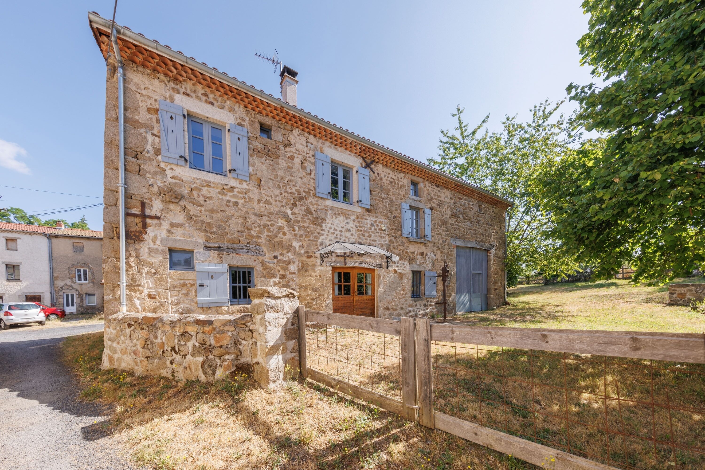 A stone building with a wooden door, windows with shutters, and a fenced yard.