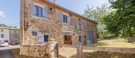 A stone building with a wooden door, windows with shutters, and a fenced yard.