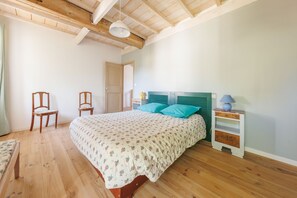 Ein Schlafzimmer mit Holzbalkendecke, einem Bett mit Blumenmuster-Bettwäsche, zwei Stühlen, einem Nachttisch mit Lampe und einem Kleiderschrank.