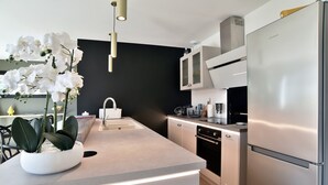 A modern kitchen with a central island, stainless steel appliances, and a black accent wall. - Ker Siméon - Maison moderne à 600 m de la plage (Saint-Cast-le-Guildo)