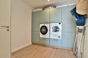 A laundry room with two washing machines, a drying rack, and a cabinet with a baby item on top. - Ker Siméon - Maison moderne à 600 m de la plage (Saint-Cast-le-Guildo)