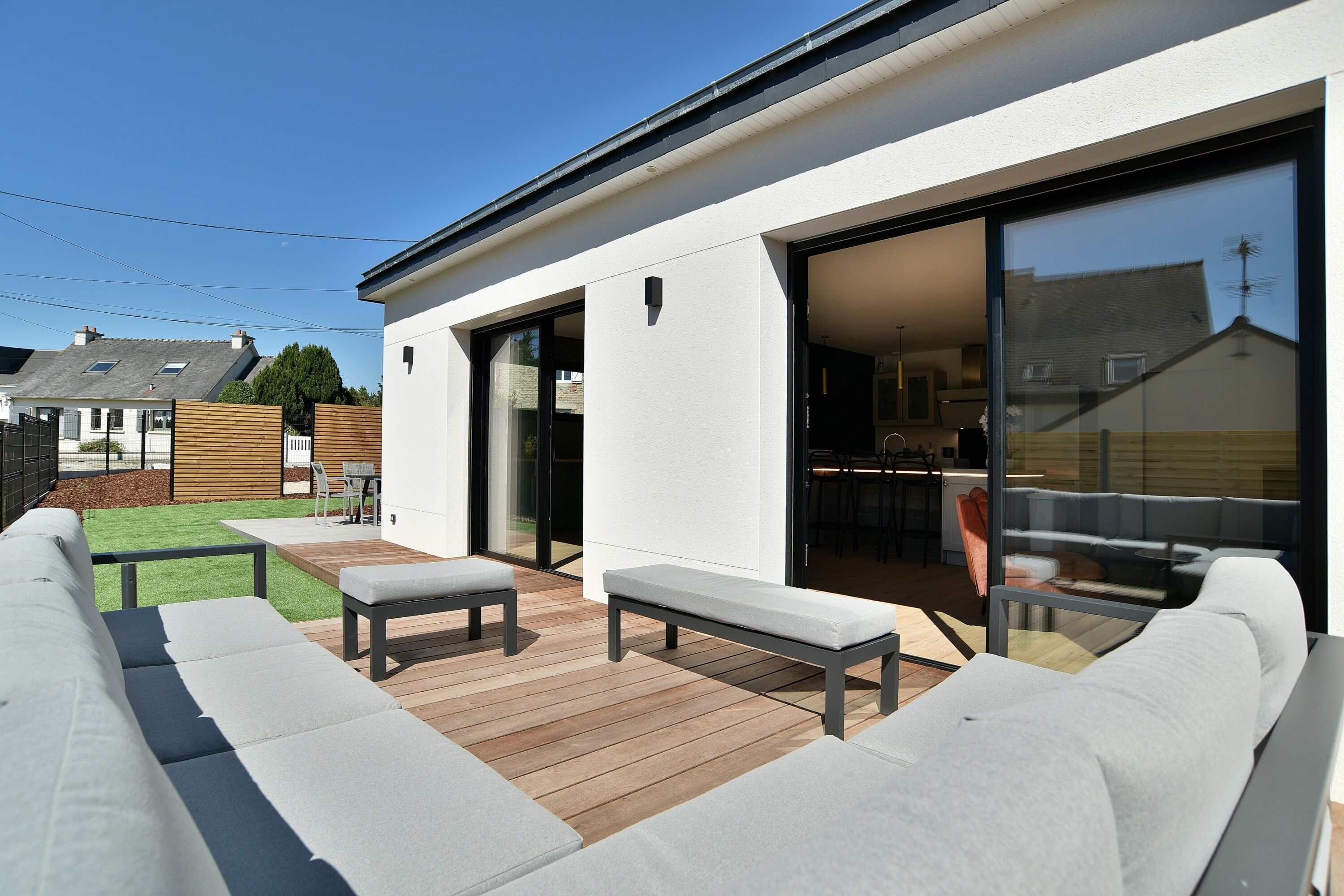 A modern outdoor patio with a wooden deck, built-in seating, and a glass door leading to an interior space.