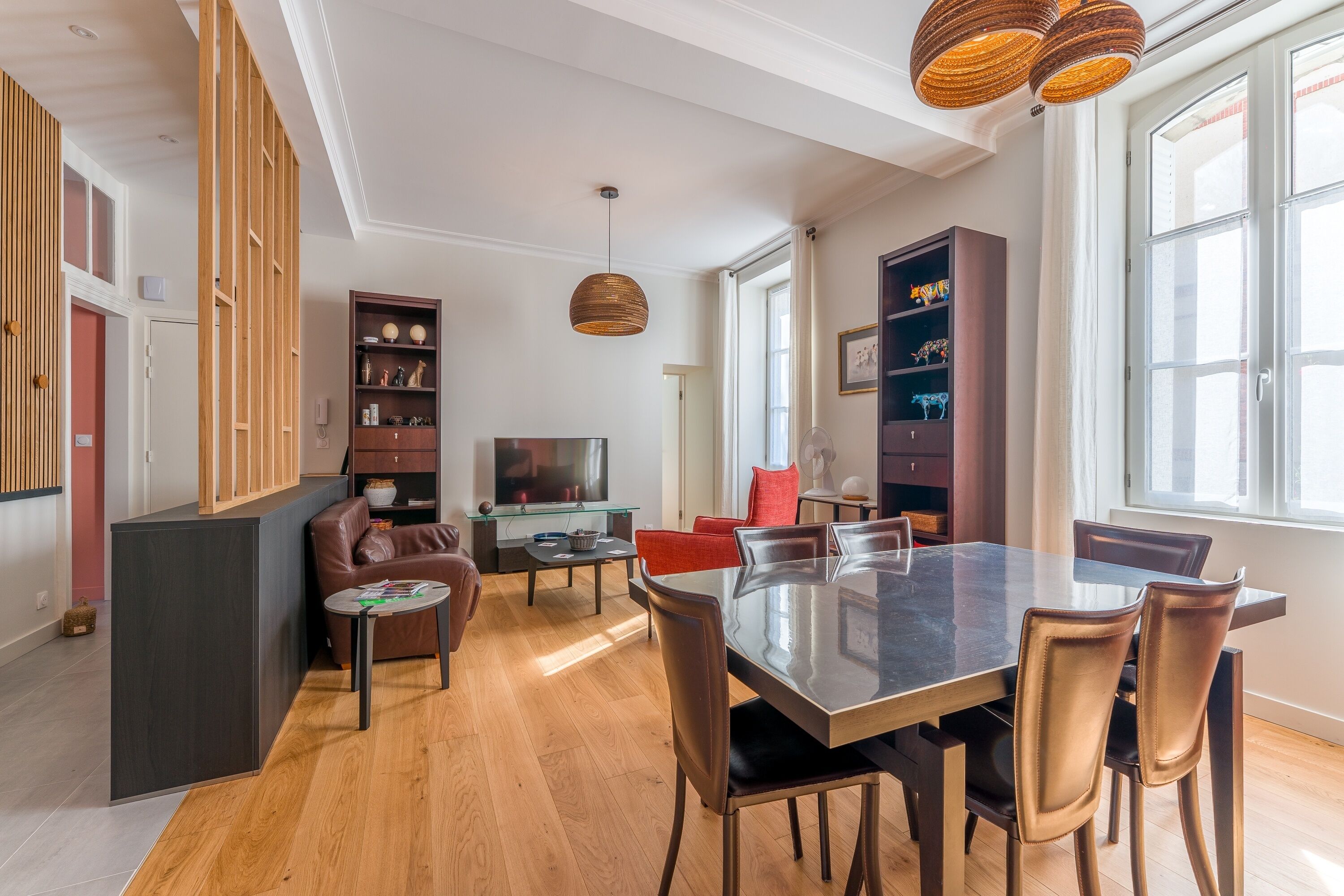 Een moderne woonkamer met een eethoek, houten lambrisering, een televisie en een groot raam.