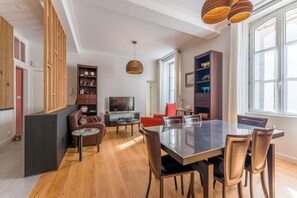A modern living room with a dining area, wooden paneling, a TV, and a large window. - Châteaubriand - Appt pour 4 au cœur de Nantes (Nantes)
