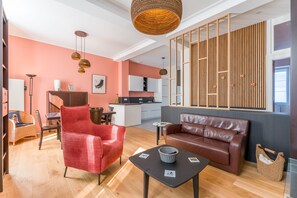 A modern living room with a red chair, a brown sofa, a small table, and a kitchen in the background. - Châteaubriand - Appt pour 4 au cœur de Nantes (Nantes)