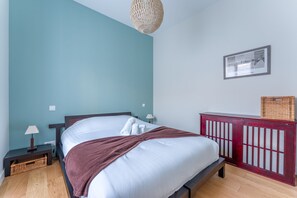 A bedroom with a bed, a nightstand, a lamp, a wall-mounted picture, and a wooden floor. - Châteaubriand - Appt pour 4 au cœur de Nantes (Nantes)