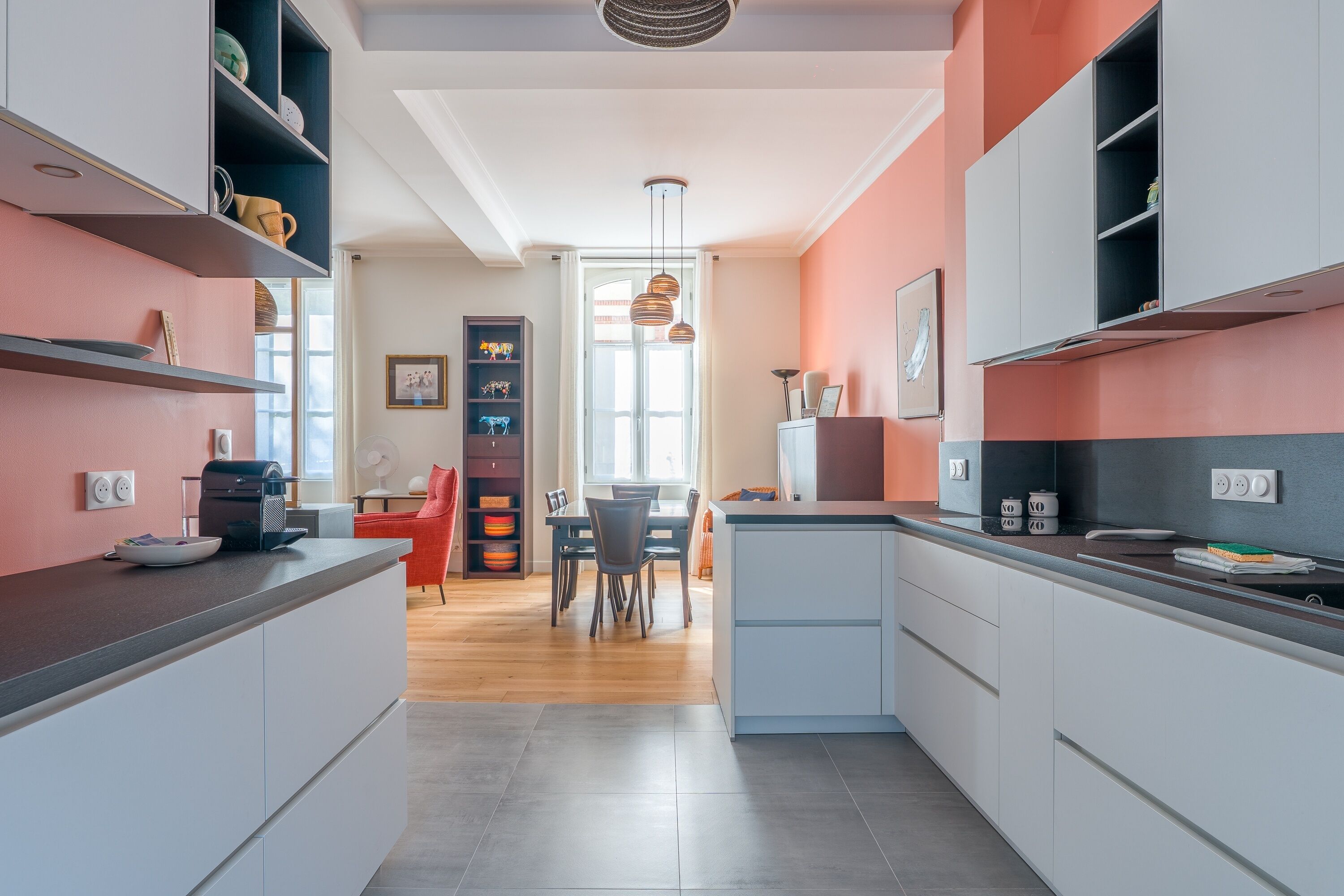 A modern kitchen with grey cabinets, a dining area with a red chair, and a view to the dining room.