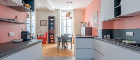 A modern kitchen with grey cabinets, a dining area with a red chair, and a view to the dining room.