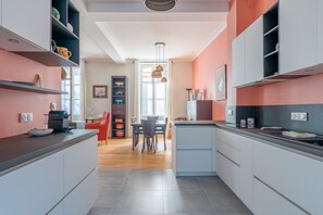 A modern kitchen with grey cabinets, a dining area with a red chair, and a view to the dining room. - Châteaubriand - Appt pour 4 au cœur de Nantes (Nantes)