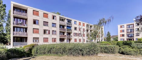 Un immeuble résidentiel à plusieurs étages, doté de balcons, avec un ciel dégagé et entouré de verdure.