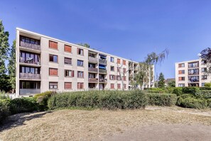 Ein mehrstöckiges Wohngebäude mit Balkonen, blauem Himmel und umgebender Bepflanzung.