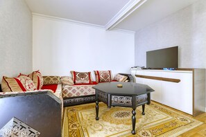 Ein Wohnzimmer mit einer Sofagarnitur, einem Couchtisch, einem Fernseher und einem gemusterten Teppich.