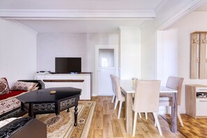 A modern living room with a flat-screen TV, a dining table with chairs, a sofa, and a small cabinet. - Louis Choix - À 1 km de la gare Garges (Garges-les-Gonesse)