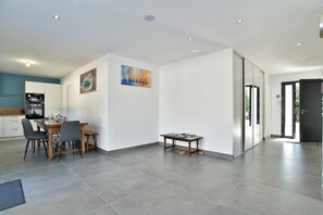 A modern kitchen with a dining area, a painting on the wall, and a sliding door leading to another room. - Ti Kastrilhez - Appt pour 6 avec terrasse & jardin (Saint-Cast-le-Guildo)