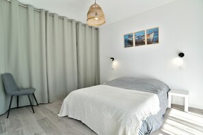 Une chambre à coucher comprenant un lit, une chaise, une table de chevet, un luminaire suspendu et deux lampes fixées au mur.
