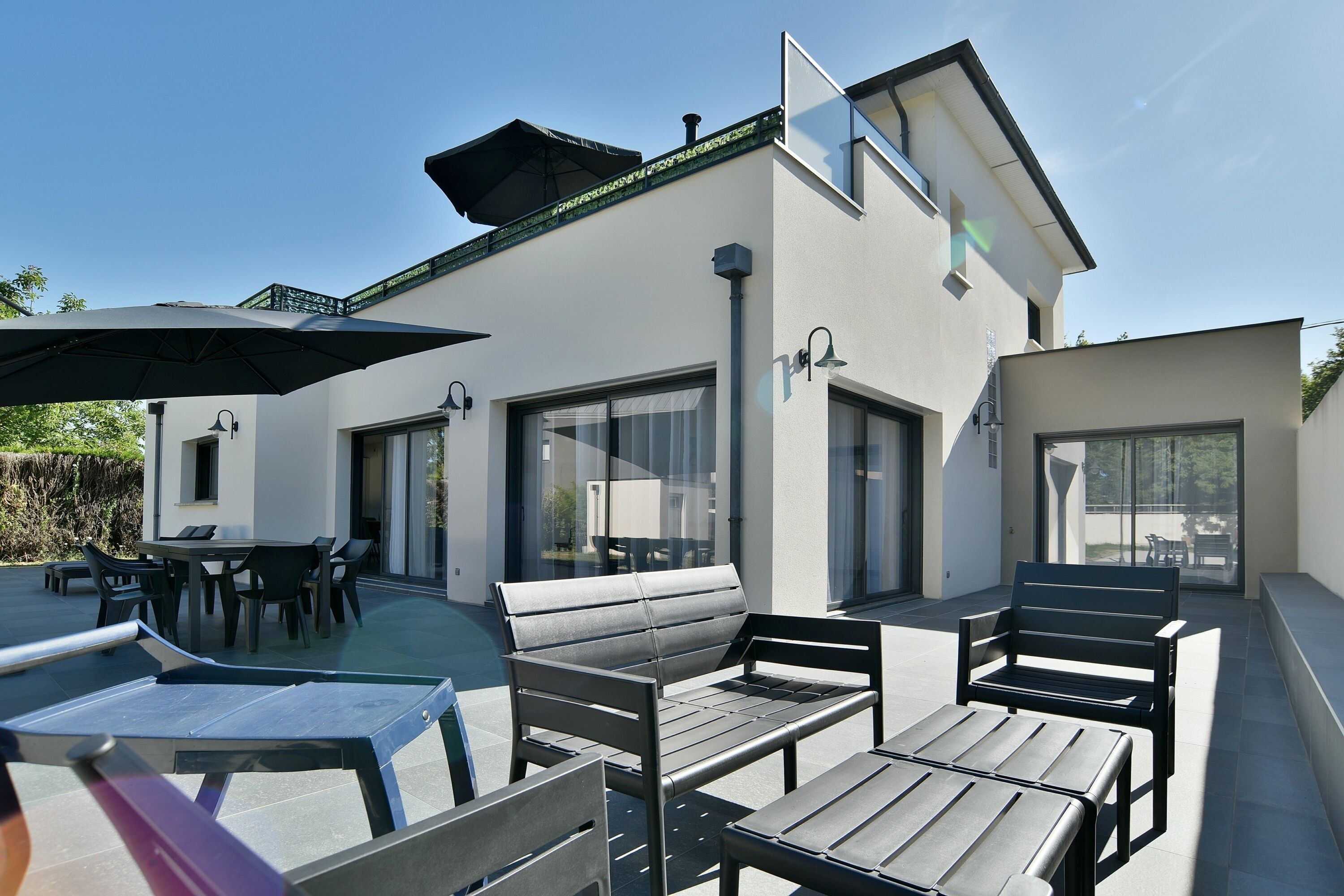 Ein modernes Haus mit Terrasse, Gartenmöbeln, einem Pool und großen Fenstern.