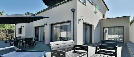 Una casa moderna con un patio que tiene mobiliario exterior, una piscina y ventanas grandes.