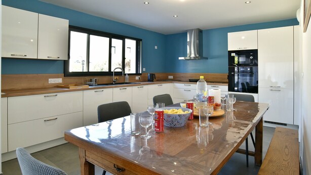 Une cuisine moderne avec des meubles blancs, une table à manger en bois et une grande fenêtre.