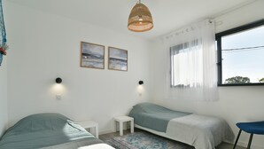 A bedroom with two beds, a small table, a chair, a window with curtains, and two wall-mounted lights. - Ti Kastrilhez - 1er - À 1 km de la plage (Saint-Cast-le-Guildo)