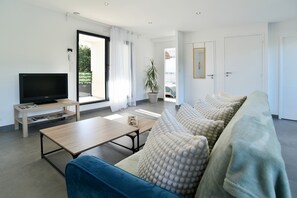 Ein modernes Wohnzimmer mit Flachbildfernseher, einer Couch, einem Couchtisch und einer Glastür, die zu einem Außenbereich führt.