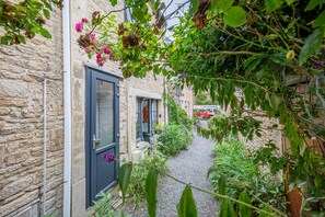 Une ruelle étroite aux murs de pierre, avec une porte et un chemin de gravier.