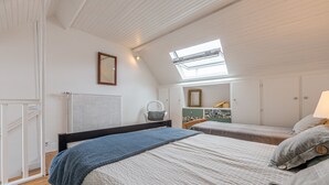 Een slaapkamer met twee bedden, een dakvenster, een radiator en een stoel.