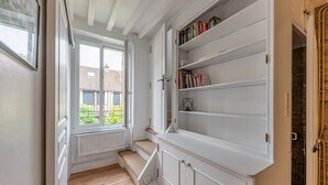 Een smalle gang met een raam, een radiator en een boekenkast vol boeken.