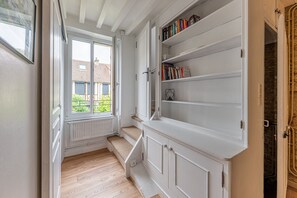 A narrow hallway with a window, a radiator, and a bookshelf with books. - Bulle de Nacre - À 250 m de la plage (Saint-Aubin-sur-Mer)