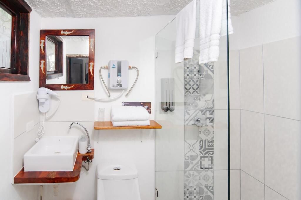 A bathroom with a sink, toilet, shower, and a mirror with a wooden frame.