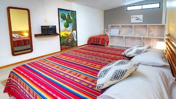 A hotel room with a large bed, a television, a painting, and a shelf with towels.