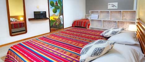 Una habitación de hotel con una cama grande, televisión, un cuadro y un estante con toallas.