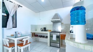 Een kleine keuken met een gasfornuis, een waterdispenser, en een eethoek met stoelen en een tafel.