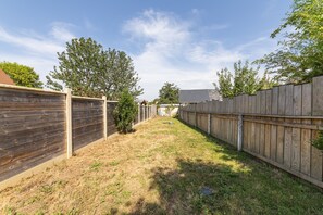 Ein Garten mit Holzzaun, einem kleinen Baum und einer Rasenfläche.