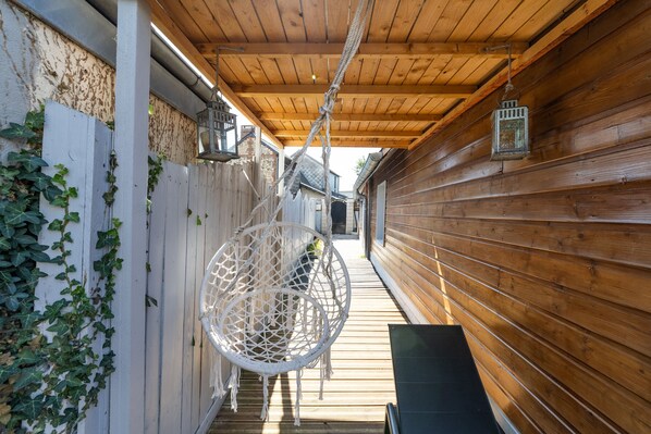 A wooden exterior with a hanging chair, a white fence, and a wooden deck.