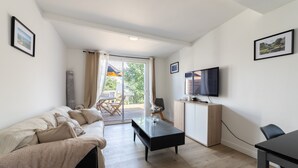Ein modernes Wohnzimmer mit Sofa, Couchtisch, Fernseher und einer Glastür, die zu einem Außenbereich führt.