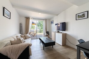 Ein modernes Wohnzimmer mit Sofa, Couchtisch, Fernseher und einer Glastür, die zu einem Außenbereich führt.