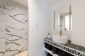 Une salle de bain avec un mur en marbre blanc, un lavabo rond doté d’un robinet doré et un miroir au-dessus.