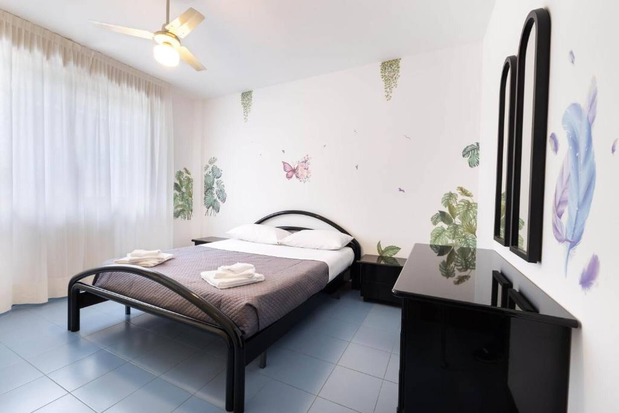 Un dormitorio con cama, escritorio, ventilador de techo y decoración en las paredes.