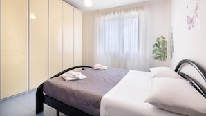 A bedroom with a bed, a ceiling fan, a window with curtains, and a wall with a plant and butterfly decoration. - Charming 3-bedroom Apartment in Riccione With Free Parking (Riccione)