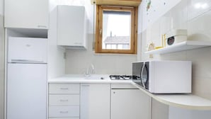 A compact kitchen with white cabinetry, a built-in microwave, a gas stove, and a small window. - Charming 3-bedroom Apartment in Riccione With Free Parking (Riccione)