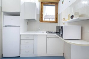 Eine kompakte Küche mit weißen Schränken, einer eingebauten Mikrowelle, einem Gasherd und einem kleinen Fenster.