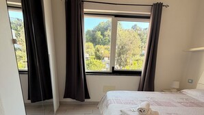 A bedroom with a bed, a window with curtains, a mirror, and a view of trees and buildings. - CASA al centro di Lacco Ameno: a piedi alle terme Negombo, mare e ristoranti (Lacco Ameno)